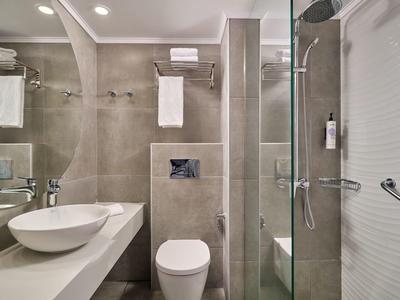 Modern bathroom with glass shower, white toilet, and sink on gray tiles.