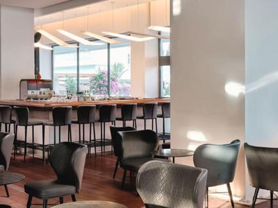 Modern hotel bar area with high bar stools and seating overlooking a terrace.