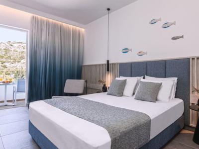 Modern hotel room with double bed, gray pillows, sea decor, and balcony with sea view.