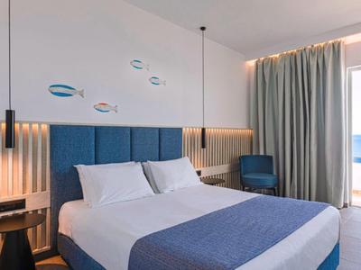 Modern hotel room with double bed, blue accents, and large window with curtains.