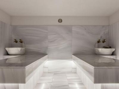 Moderner Wellnessbereich mit zwei Marmorliegen und Wandwaschbecken in neutralen Tönen.
