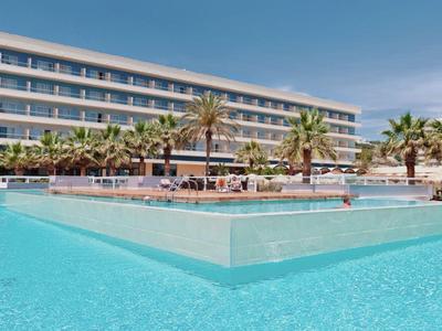 Moderner Hotelkomplex mit großem Außenpool, Palmen und blauem Himmel im Hintergrund.