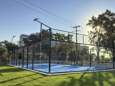 Moderner Paddle-Tennisplatz mit Glaswänden und umgeben von grüner Wiese bei Sonnenuntergang.