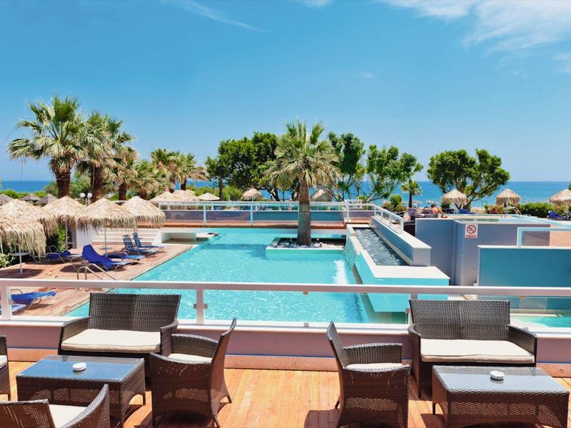 Modern hotel pool area with sun umbrellas, loungers, and palm trees under a blue sky