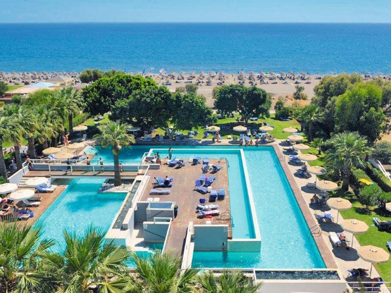 Large hotel pool with lounge chairs and a view of the beach and sea in the background.