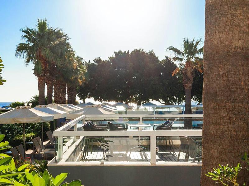 Sunny outdoor area with tables, chairs, and palm trees at a hotel beach.