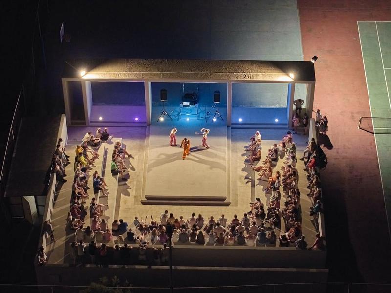 Illuminated outdoor event with stage and seated audience next to a tennis court