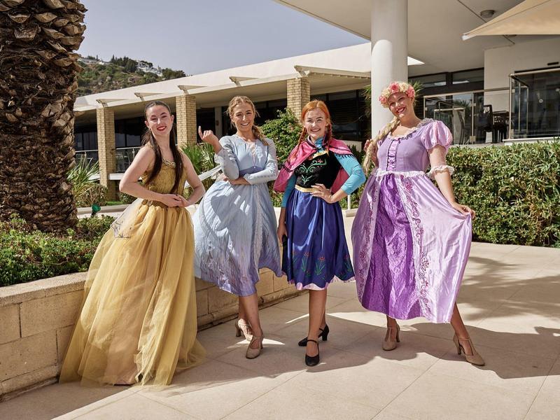 Four women in colorful dresses posing outdoors in front of a modern building.
