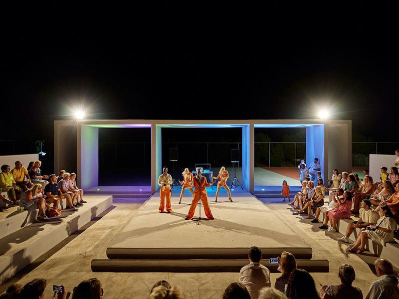 Outdoor stage at night with audience, featuring three dancers in colorful costumes