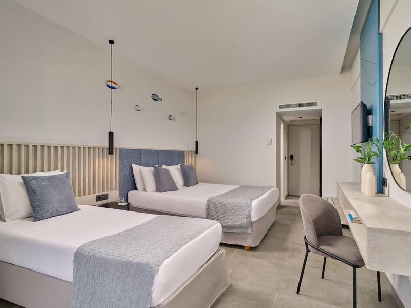 Modern hotel room with two beds, desk, and minimalist decor in neutral tones.