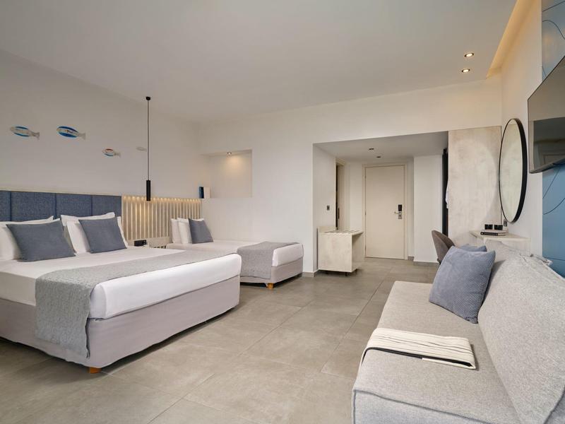 Modern hotel room with large bed, sofa, TV, and minimalist decor.