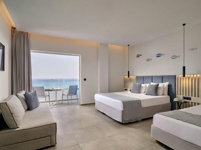 Bright hotel room with two beds, sofa, and balcony view of the sea