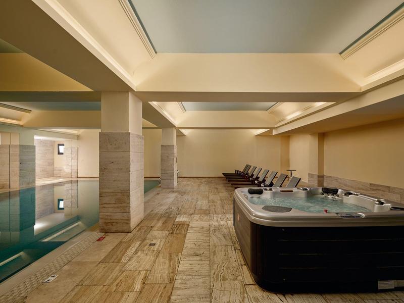 Modern wellness area with indoor pool and hot tub on light stone flooring.