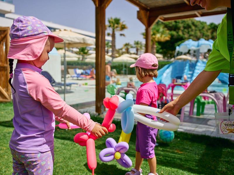 Children playing with colorful balloon animals on a sunny hotel lawn.