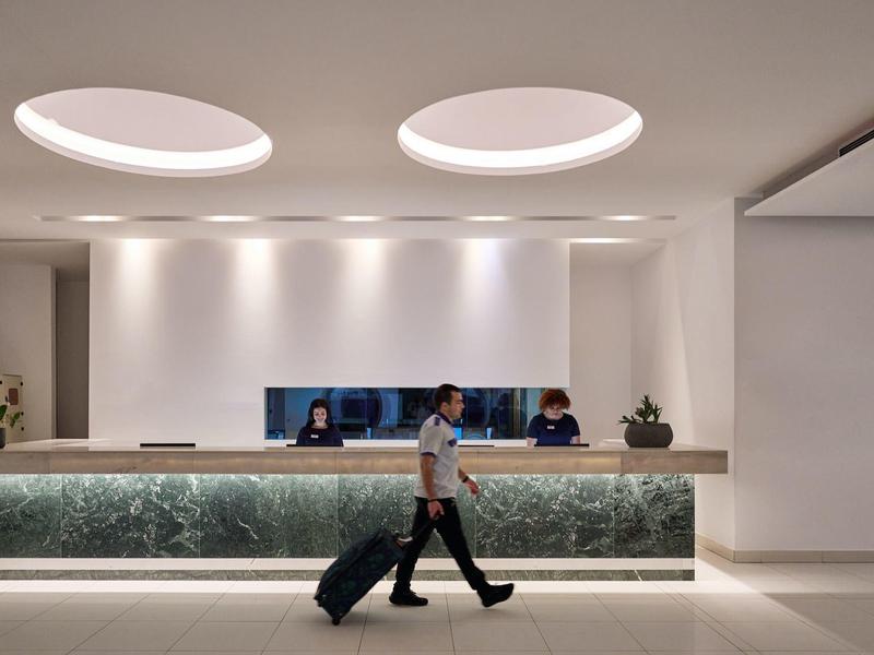 Modern hotel lobby with illuminated front desk and person pulling a suitcase