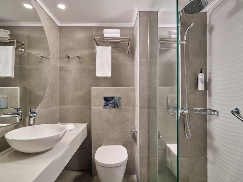 Modern bathroom with glass shower, white toilet, and sink on gray tiles.