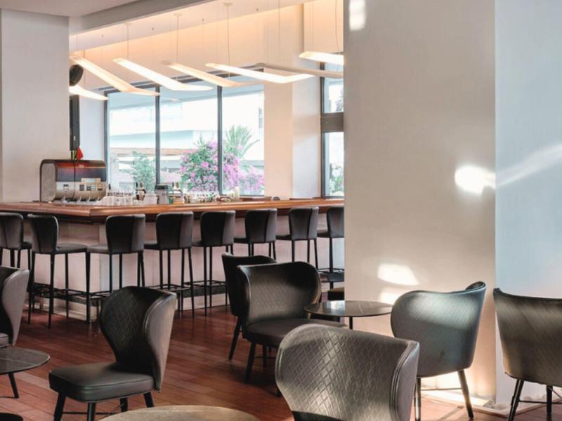 Modern hotel bar area with high bar stools and seating overlooking a terrace.