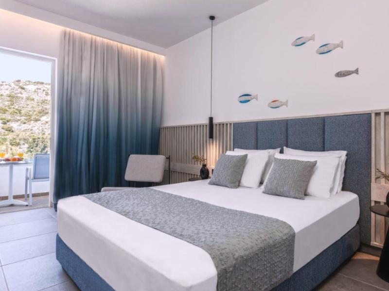Modern hotel room with double bed, gray pillows, sea decor, and balcony with sea view.
