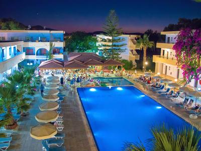 Oświetlony basen hotelowy z leżakami i tropikalnymi roślinami nocą.