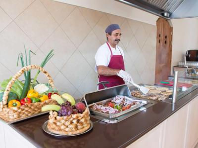 Kuchař v bílé uniformě a červené zástěře připravuje jídlo u bufetu s čerstvou zeleninou a masem.