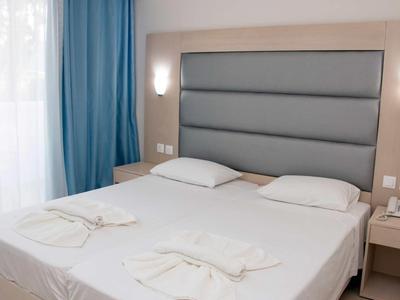 Moderní hotelový pokoj se dvěma jednolůžky, šedým čelem postele a modrými závěsy.