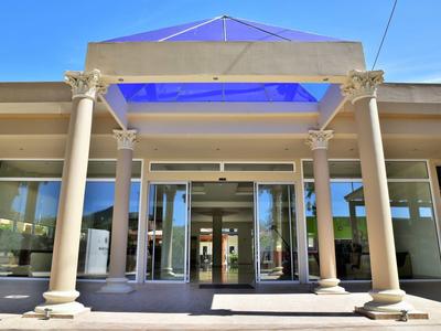 Facciata di un hotel con colonne e porte di vetro sotto un cielo blu.