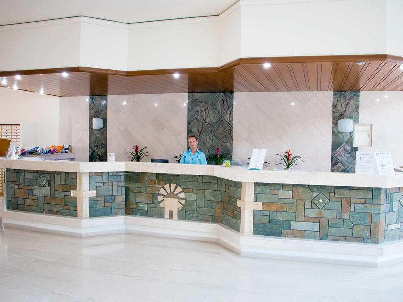 Světlá hotelová recepce s kamenným pultem a dvěma zaměstnanci.