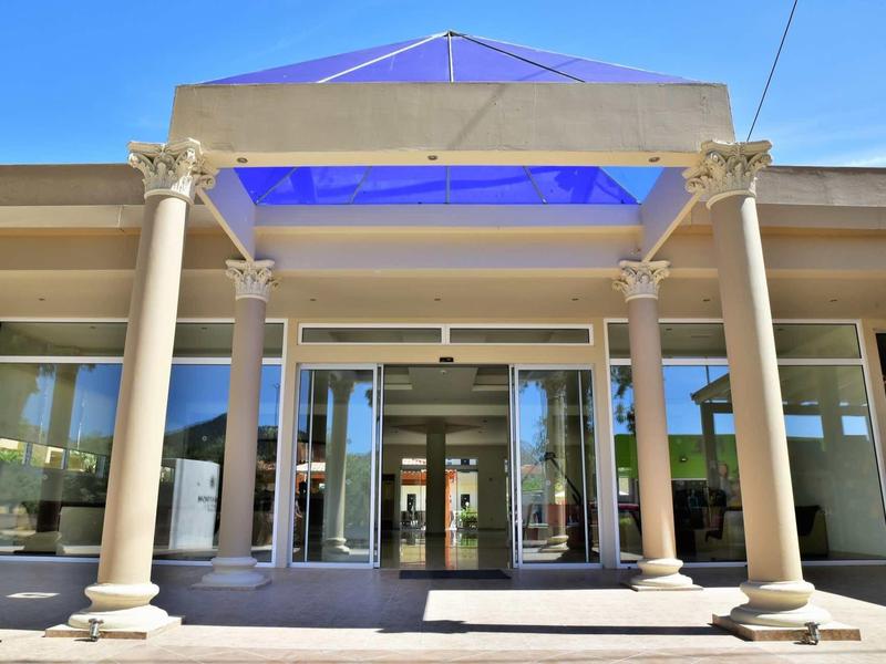 Fasáda hotelu se sloupy a skleněnými dveřmi pod modrou oblohou.