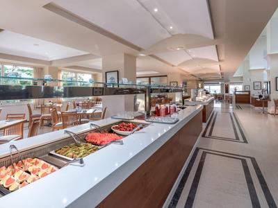 Sala colazione moderna con buffet, pareti luminose e grandi finestre.