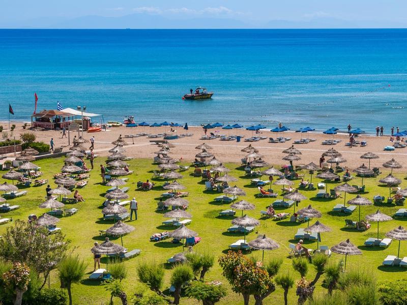 Pláž s deštníky a lehátky před modrým mořem a čistou oblohou