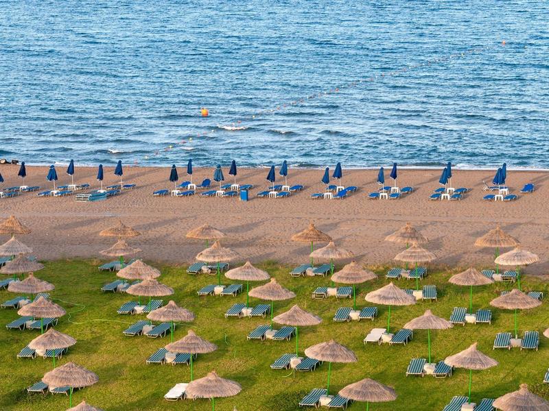 Pohled na klidnou pláž s řadami slámy slunečníky a lehátky u moře.