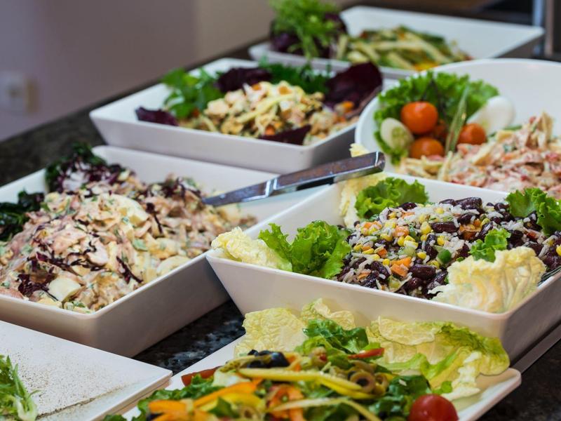 Nádržky s různými čerstvými saláty na bufetu.
