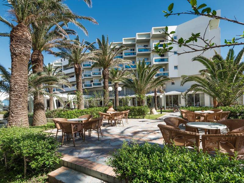 Hotelová terasa se stoly, židlemi, palmami a jasnou modrou oblohou v pozadí.