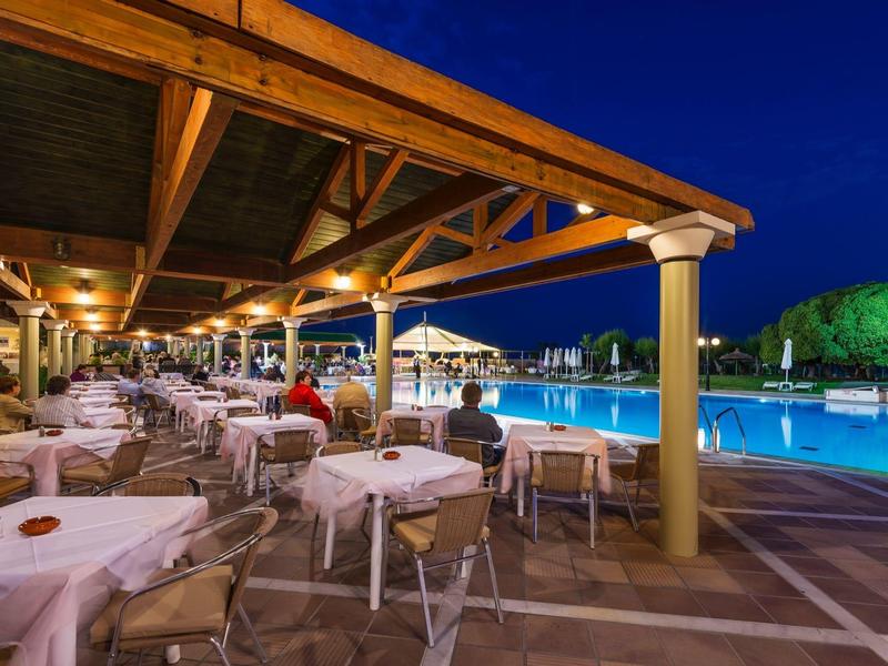 Večerně osvětlená hotelová terasa s prostřenými stoly vedle velkého bazénu.