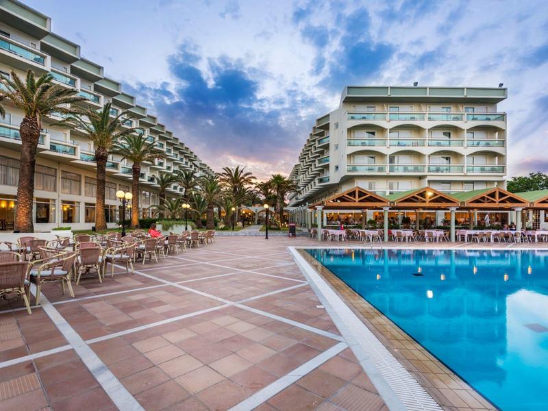 Venkovní prostor hotelu s bazénem, slunečníky a posezením za soumraku.