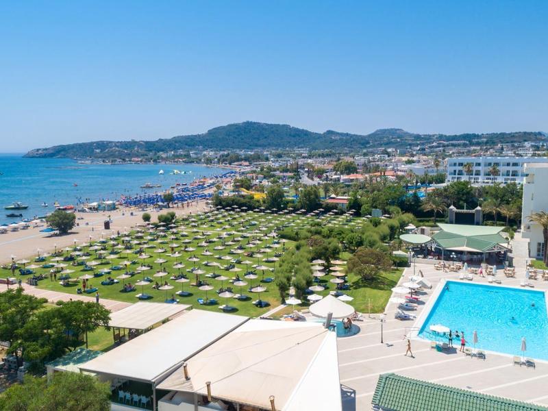 Pohled na hotelový bazén a dlouhou písečnou pláž pod jasně modrou oblohou