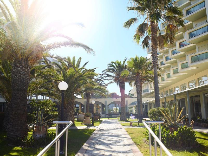 Slunná cesta v hotelu s palmami vedoucí k vchodu.