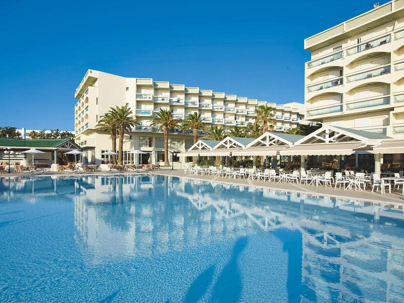 Velký hotelový bazén s lehátky a slunečníky pod modrou oblohou.