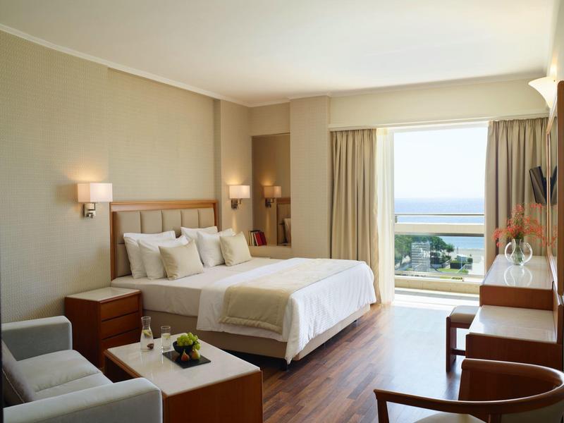 Světý hotelový pokoj s manželskou postelí, posezením a balkonem s výhledem na moře.