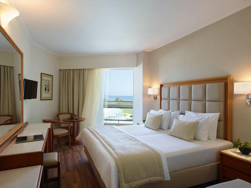 Světlý hotelový pokoj s velkou postelí, psacím stolem a výhledem na terasu