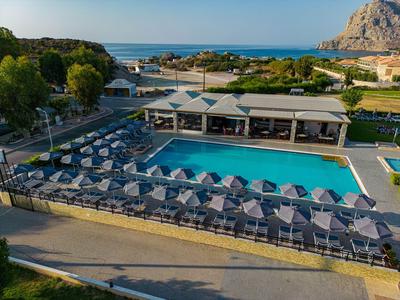 Gran piscina exterior con filas de sombrillas y tumbonas, rodeada de vegetación y vista al mar.