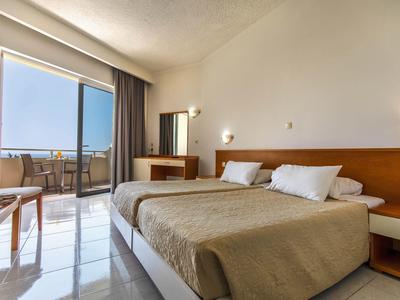 Helles Hotelzimmer mit Doppelbett, Balkon, Fensterfront, Stühlen und warmen Holzdetails.