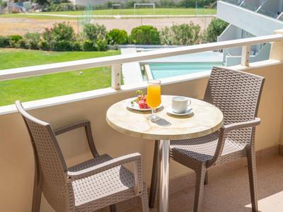 Balkon mit kleinem runden Tisch, zwei Stühlen, Orangensaft, Tasse und Bergblick im Hintergrund.