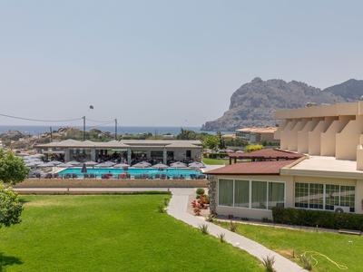 Complejo hotelero con piscina al aire libre, sombrillas y tumbonas cerca de un paisaje montañoso junto al mar.