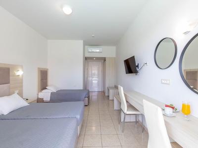 Habitación de hotel luminosa con dos camas individuales, escritorio blanco y espejo redondo.