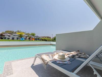 Modernes Schwimmbad mit Liegestuhl, Sonnenhut und Blick auf weiße Häuser und blauen Himmel.