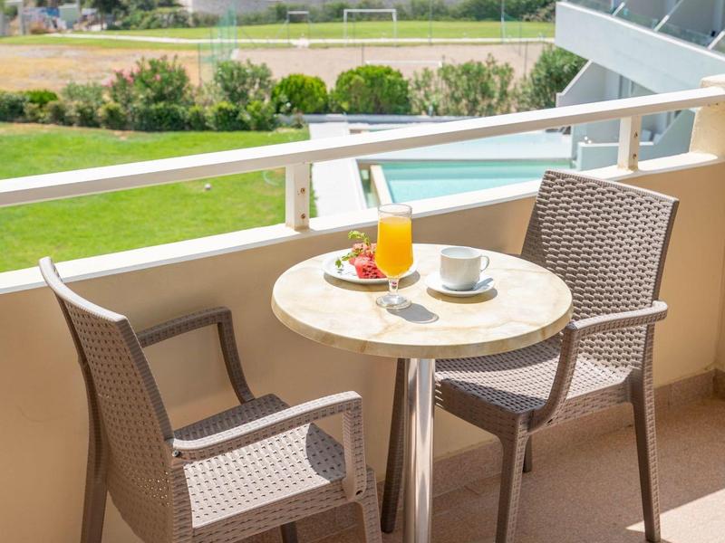 Balkon mit kleinem runden Tisch, zwei Stühlen, Orangensaft, Tasse und Bergblick im Hintergrund.