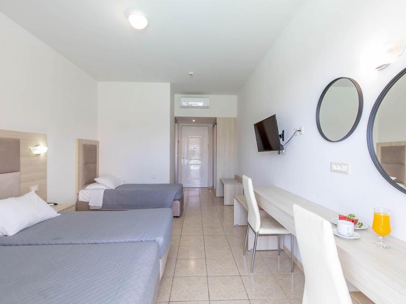 Helles Hotelzimmer mit zwei grauen Betten, weißen Wänden, Spiegeln, Schreibtisch und Flachbildfernseher.