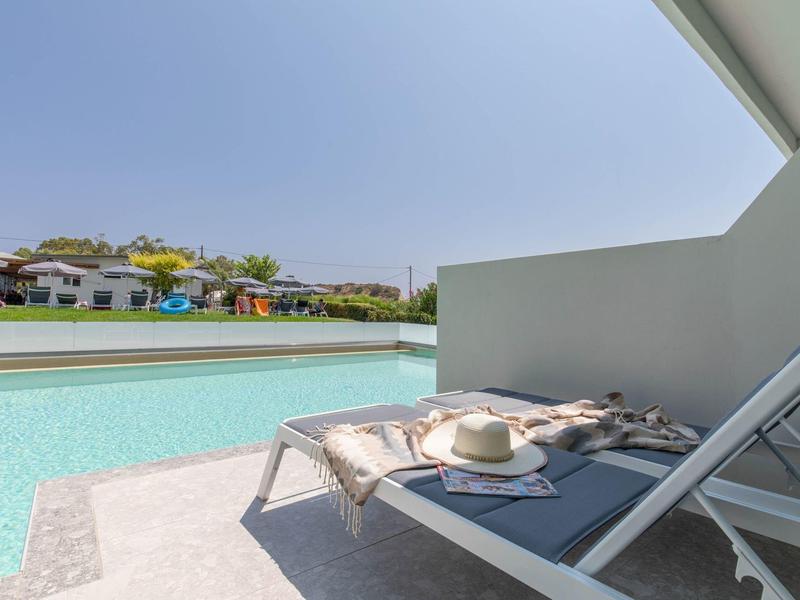 Modernes Schwimmbad mit Liegestuhl, Sonnenhut und Blick auf weiße Häuser und blauen Himmel.