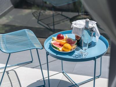 Tavolo blu con piatto di frutta e bevande accanto a sedia blu all'aperto, parzialmente visibile attraverso una tenda bianca